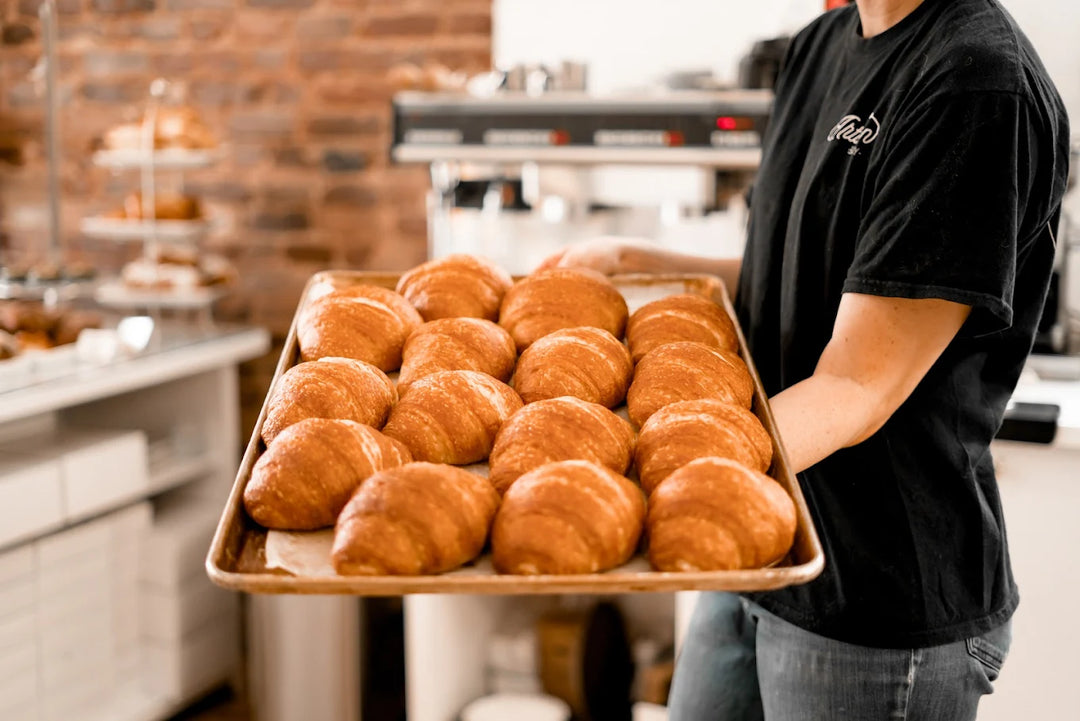 Person holding a tray of croissants in a bakery setting