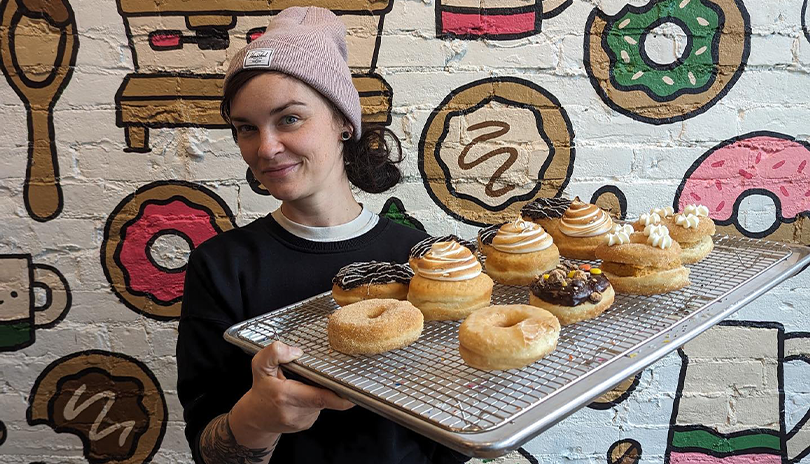 Person holding a tray of donuts in front of a colorful mural