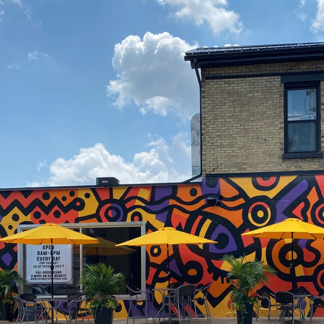 Colorful mural on a building with yellow umbrellas and chairs underneath.