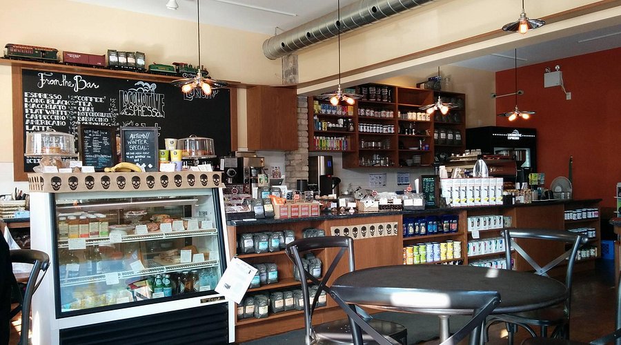 Interior of a coffee shop with tables, chairs, and a refrigerator.